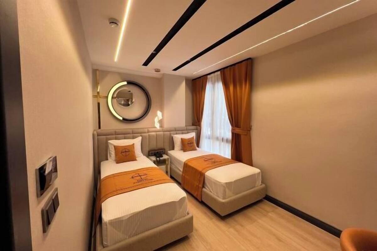 Habitación de hotel con dos camas, un espejo redondo, una mesita de noche y una ventana con cortinas.
