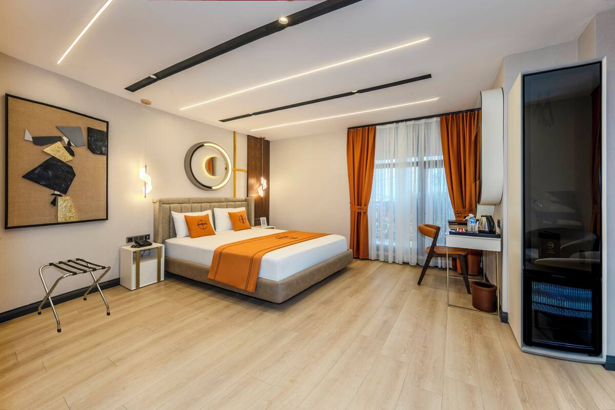 Una habitación de hotel moderna con cama, escritorio y un amplio ventanal con cortinas.