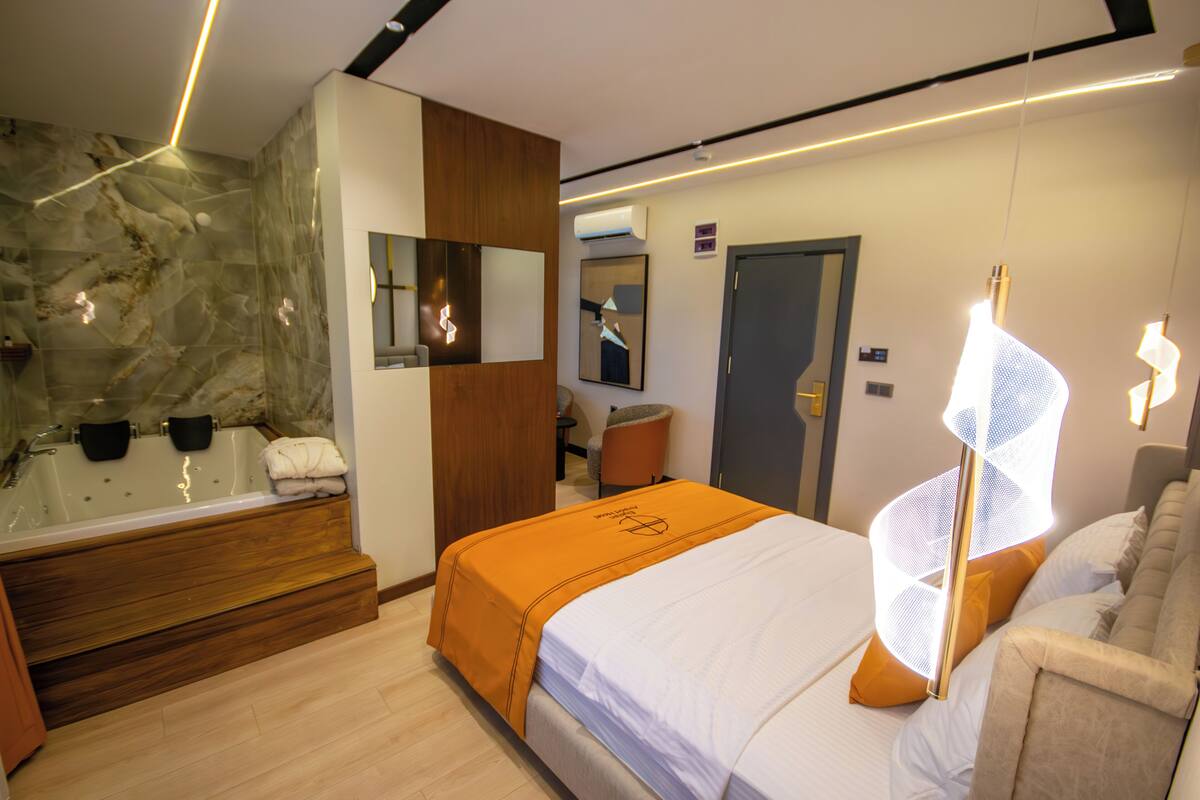 Habitación de hotel moderna con una cama grande, un baño separado con bañera y una zona de estar con una silla y una mesa.