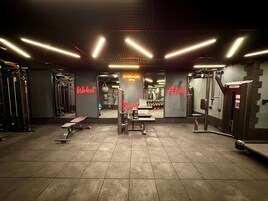 Un gimnasio con diversos equipos de ejercicio, una banca y letreros de neón motivacionales.