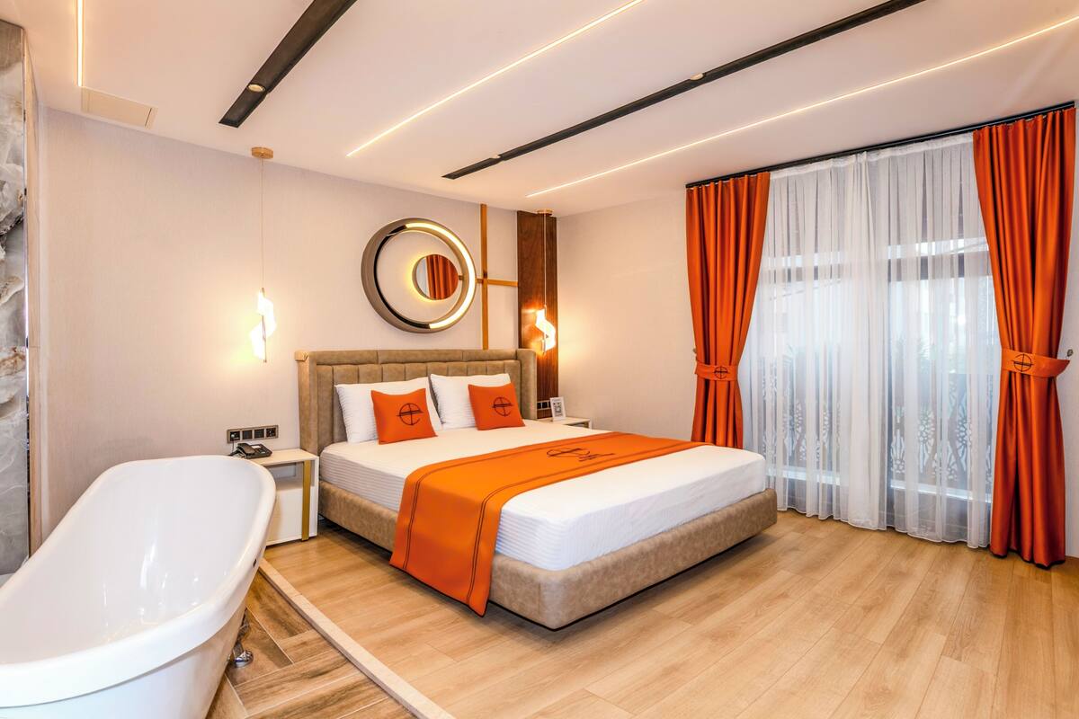 Un dormitorio moderno con una cama grande, una bañera y un ventanal con cortinas.