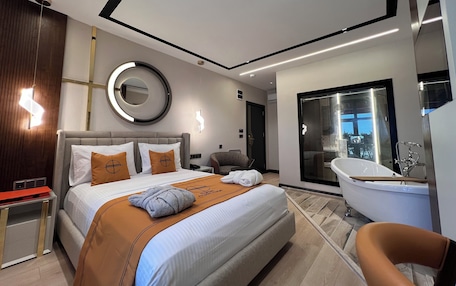 A modern hotel room with a large bed, a round mirror, a built-in bathtub, and a separate seating area.