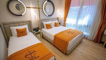 Une chambre d’hôtel avec deux lits, chacun recouvert d’une couvre-lit orange et agrémenté d’oreillers assortis. Deux miroirs ronds sont accrochés aux murs, et la chambre est dotée d’un plancher en bois.
