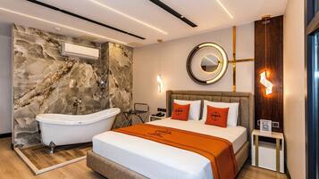 Ein modernes Hotelzimmer mit Marmorwand, einer Badewanne, einem Bett mit orangefarbener Bettwäsche, einem runden Spiegel und einem Nachttisch mit einem QR-Code.