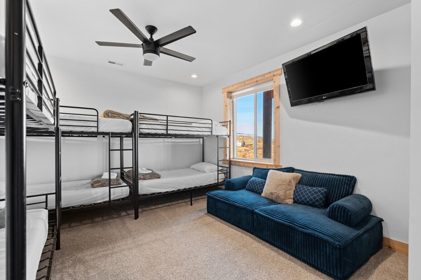 Une chambre avec des lits superposés, un ventilateur de plafond, un téléviseur fixé au mur et une fenêtre donnant sur l’extérieur.