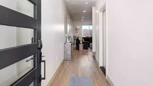 A hallway with a modern door, a small table with a vase, and a seating area in the background.