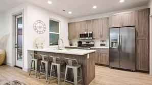 A modern kitchen with a central island, bar stools, stainless steel appliances, and wooden cabinets. - Sleeps 18! Pool! Pizza Oven! 2 Townhomes! (Santa Clara)