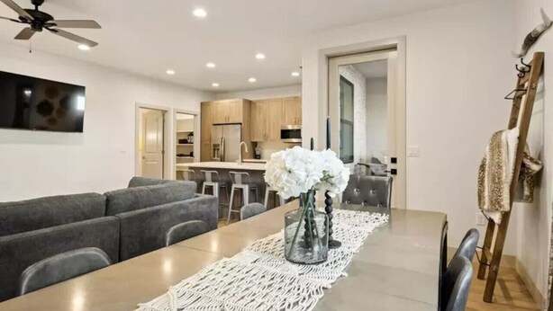 A modern dining area with a long table, grey upholstered seating, and a decorative macrame runner. - Sleeps 18! Pool! Pizza Oven! 2 Townhomes! (Santa Clara)
