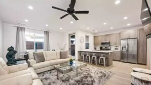 A modern living room with a sofa, coffee table, and a ceiling fan. - Sleeps 18! Pool! Pizza Oven! 2 Townhomes! (Santa Clara)