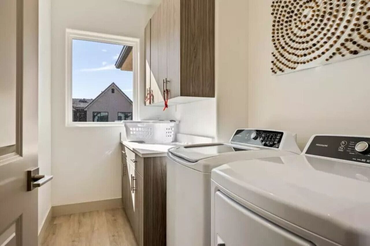 Een wasserette met een wasmachine, een droger en een raam met uitzicht op huizen.