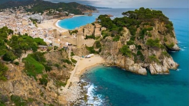 A coastal town with a beach, rocky cliffs, and a clear blue sea.