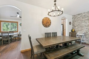 A dining area with a large wooden table, chairs, a chandelier, and a clock on the wall.
