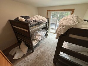 A dormitory room with two bunk beds, a sliding glass door leading to a balcony, and a carpeted floor.