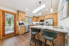 Una cocina moderna con armarios de madera, una isla grande, taburetes de bar y vistas al exterior mediante una puerta corredera.