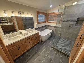 Een moderne badkamer met een douche in een glazen cabine, een vrijstaand bad en een wastafel met een grote spiegel en verlichtingsarmaturen.