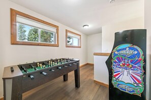 Una habitación con mesa de fútbol, dos ventanas con marcos de madera y un panel decorativo en la pared.