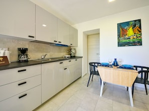 A modern kitchen with white cabinets, a coffee maker, and a dining area with a table and chairs.