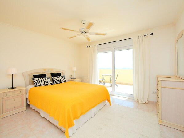 A bedroom with a bed, a ceiling fan, a nightstand, a dresser, and a view of the outside.