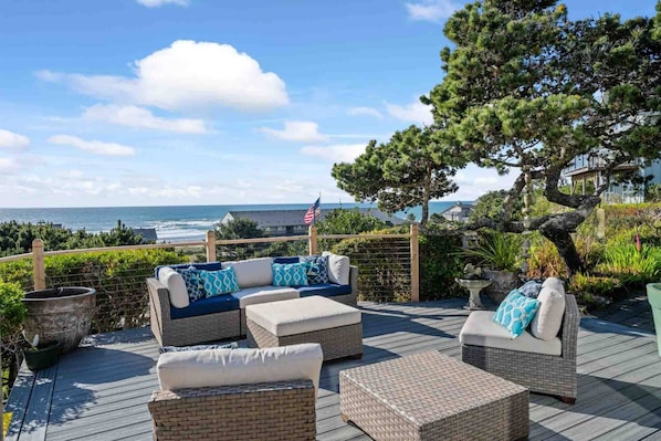 A deck with wicker furniture, a view of the ocean, and a flag.
