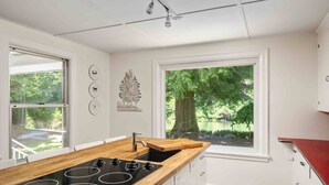 A modern kitchen with a central island, white cabinetry, and a large window offering a view of a tree and greenery. - Spectacular Riverfront Setting, Pet Friendly, EV Charger, Fire-Table, Sauna, BBQ Overlooking River (West Linn)