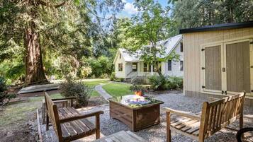 Une terrasse en bois avec un foyer, entourée d’une zone recouverte de gravier et de chaises en bois.