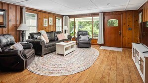 A spacious living room with a leather sofa, a coffee table, and a chair. The room has wooden paneling, large windows, and a door with a handle. - Spectacular Riverfront Setting, Pet Friendly, EV Charger, Fire-Table, Sauna, BBQ Overlooking River (West Linn)