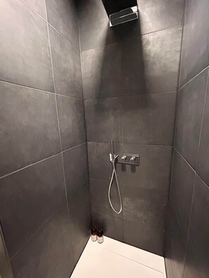 A shower with dark tiles, a handheld showerhead, and a wall-mounted control panel.