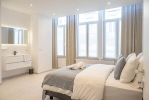 A modern bedroom with a large bed, a built-in wardrobe, and a window with curtains.
