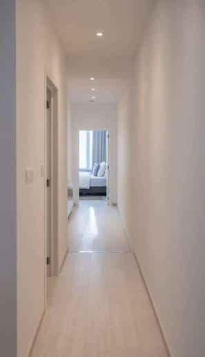 A narrow hallway with a bed at the end, white walls, and a light-colored floor.