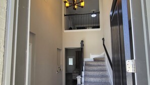 A multi-level interior with a staircase, a chandelier, and a door leading to another room.