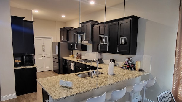 A modern kitchen with dark cabinets, a granite countertop, and a central island with bar stools.