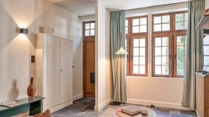 Una habitación amplia con un gran ventanal, una mesa redonda de madera, una lámpara de pie y un armario.