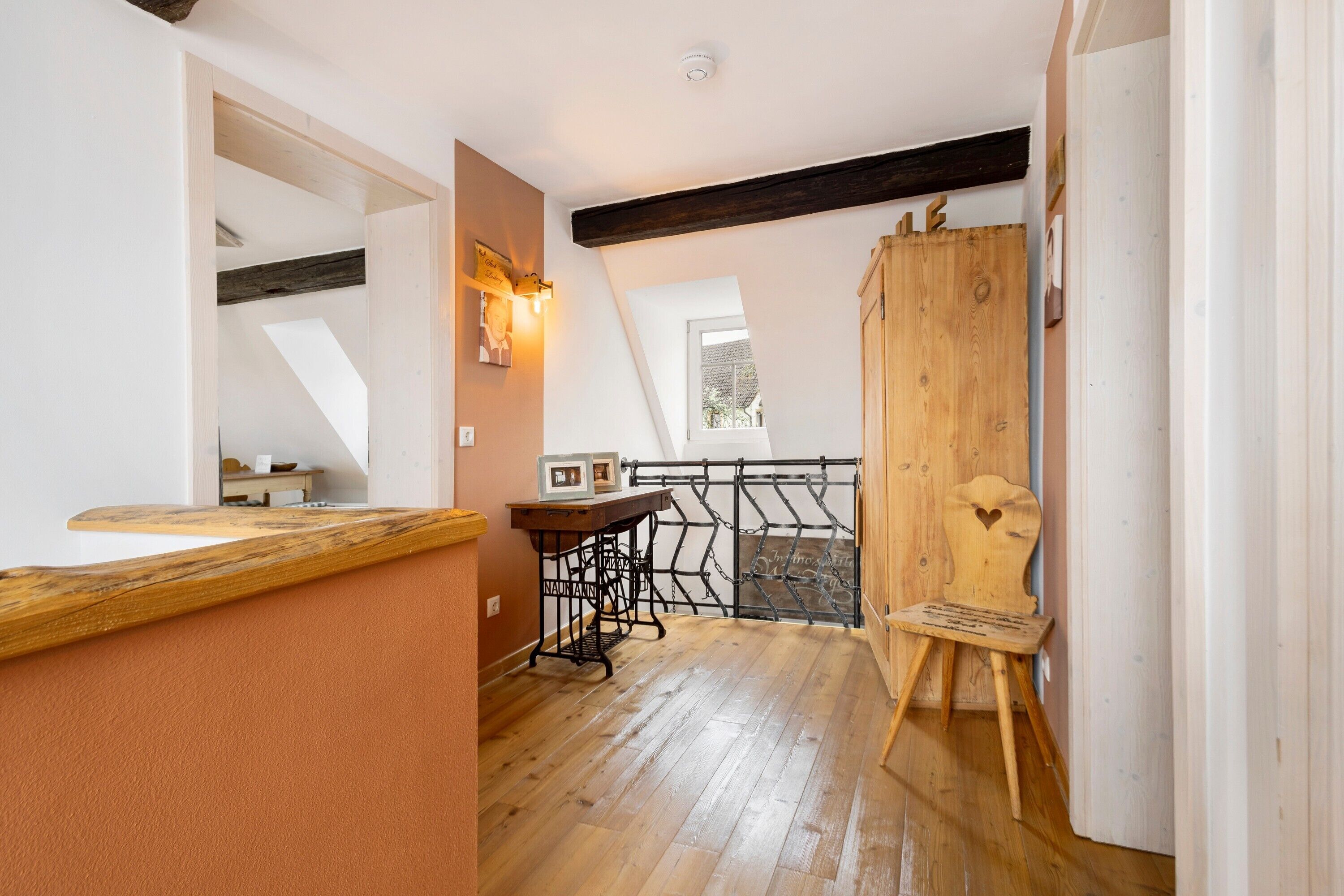Ein Loft-Zimmer mit freiliegenden Holzbalken, einer Nähmaschine, einem Holzstuhl und einem kleinen Tisch.