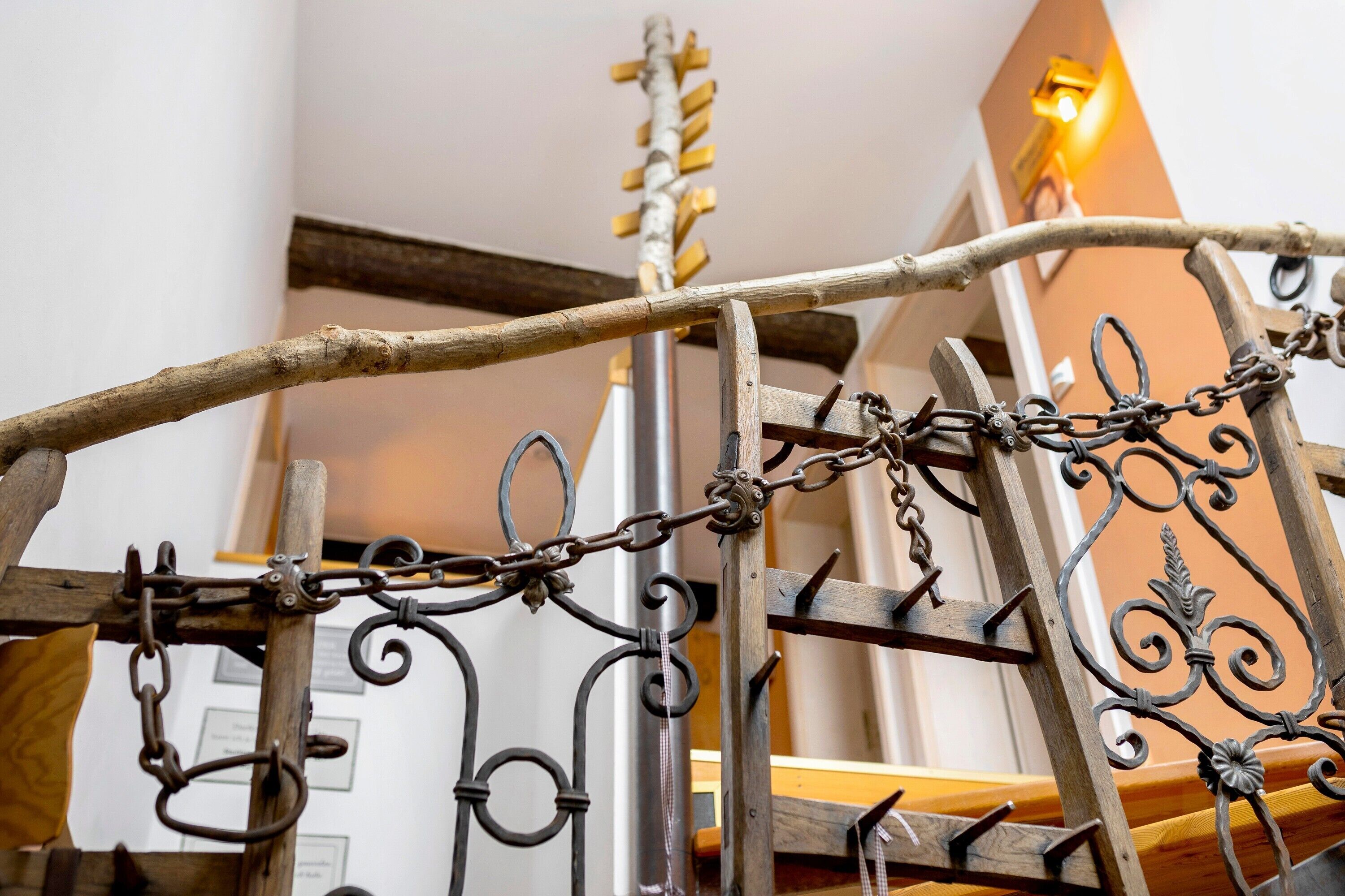 Une rampe en fer forgé ornée de motifs complexes, un poteau en bois et une chaîne métallique.