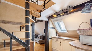 A wooden staircase with a black handrail, a loft bedroom with a skylight, and a kitchen with white cabinets. - Apartment 'Stub'n Balbine' with Shared Terrace and Wi-Fi (Waischenfeld)