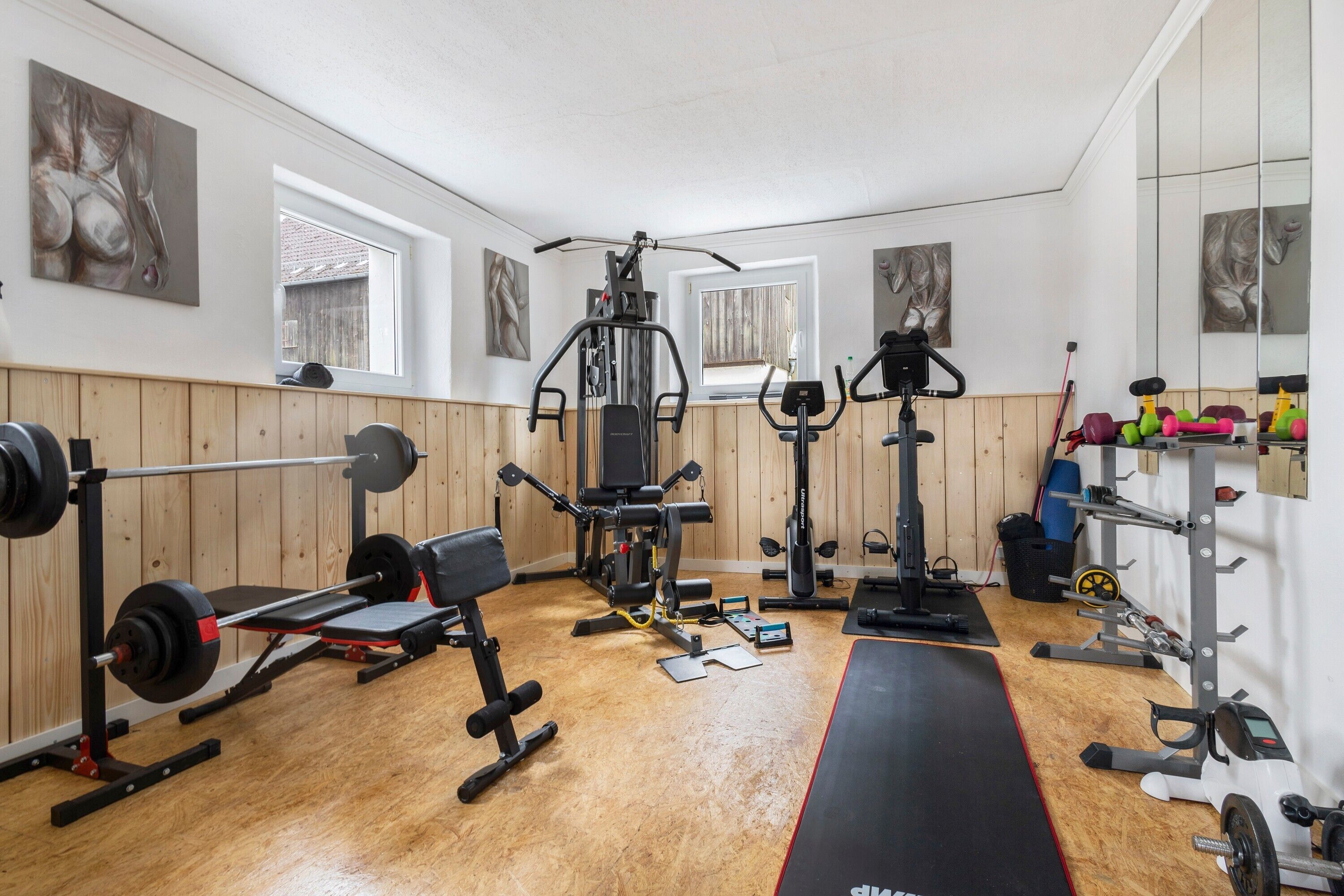 A gym with various exercise equipment, wooden walls, and windows.