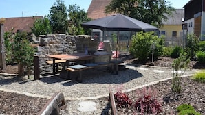 An outdoor patio with a table and chairs, a stone wall, and a garden area with plants and a gravel path. - Apartment 'Stub'n Rettl' with Shared Terrace, Shared Garden and Wi-Fi (Waischenfeld)