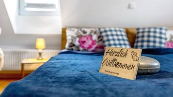 Un letto con una coperta blu, una lampada da comodino e un cartello di legno con la scritta 'Herzlich Willkommen'.