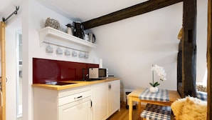 A compact kitchen with white cabinets, a red backsplash, a microwave, and a small dining table with a checkered tablecloth. - Apartment 'Stub'n Rettl' with Shared Terrace, Shared Garden and Wi-Fi (Waischenfeld)