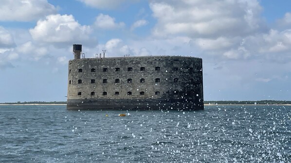 A large, cylindrical stone structure with multiple windows, situated in a body of water.