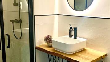 Un bagno con box doccia in vetro, un lavandino bianco con piano in legno, uno specchio rotondo e un asciugamano su un porta asciugamani.