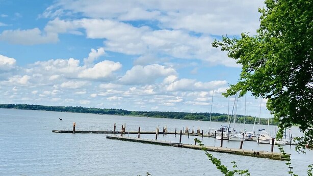 Un lac paisible avec une jetée qui s’avance sur l’eau, entouré de verdure et sous un ciel dégagé.