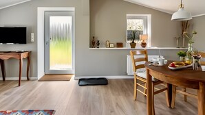 Un coin repas comprenant une table en bois, des chaises, un tapis noir, une suspension blanche et une fenêtre donnant sur un paysage.