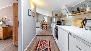 Une cuisine moderne avec des meubles blancs, un four Bosch et un coin repas comprenant une table et des chaises en bois.