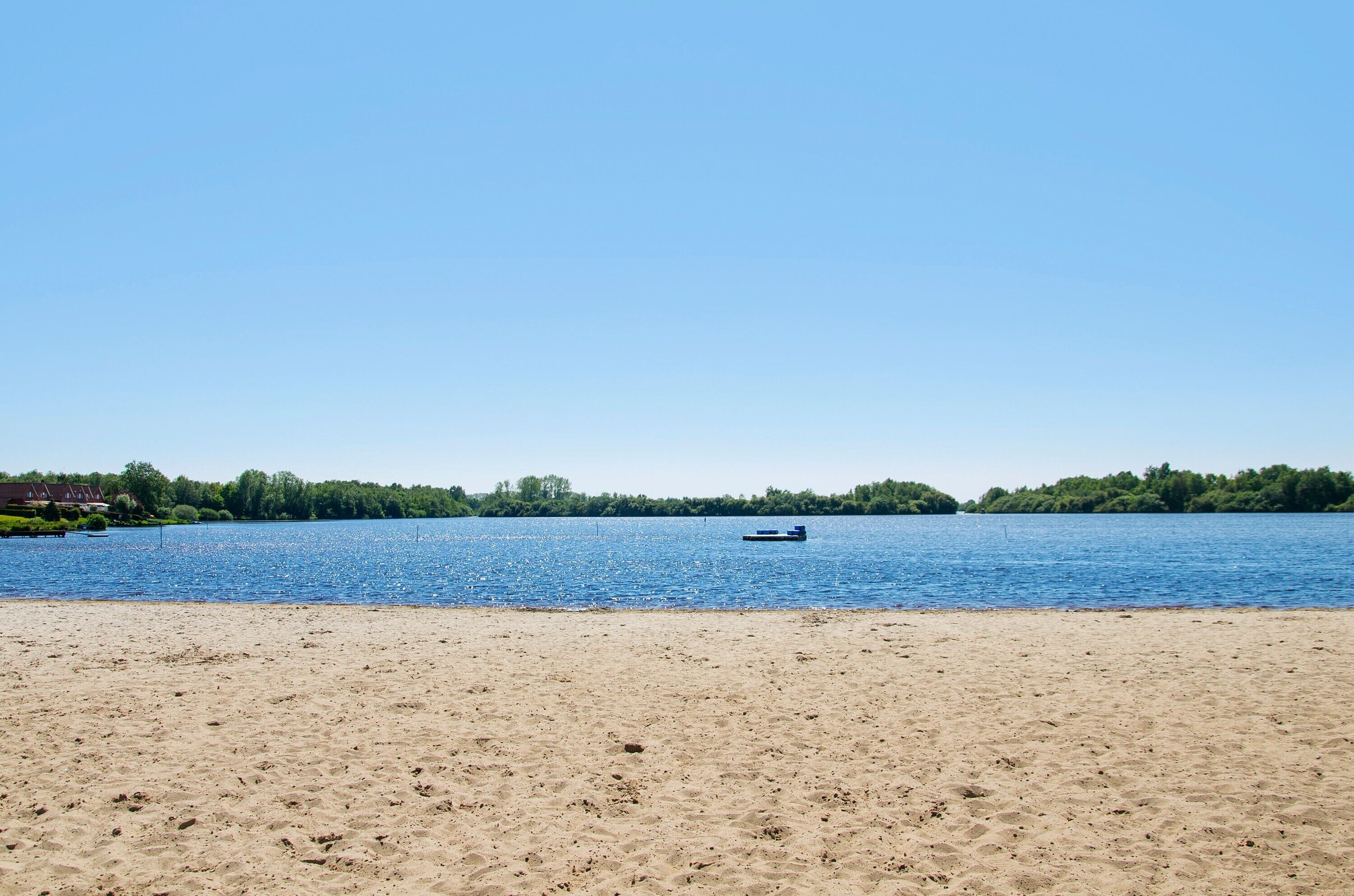 Een strand met een boot op het water, een zandstrand en een bebost gebied op de achtergrond.