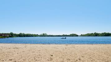 Een strand met een boot op het water, een zandstrand en een bebost gebied op de achtergrond.