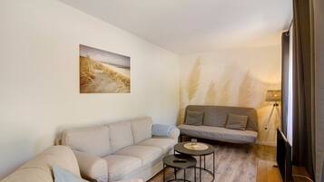 A living room with a sofa, a smaller couch, a coffee table, a lamp, and a TV.