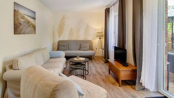A living room with a sofa, a coffee table, a TV on a wooden stand, and a lamp.