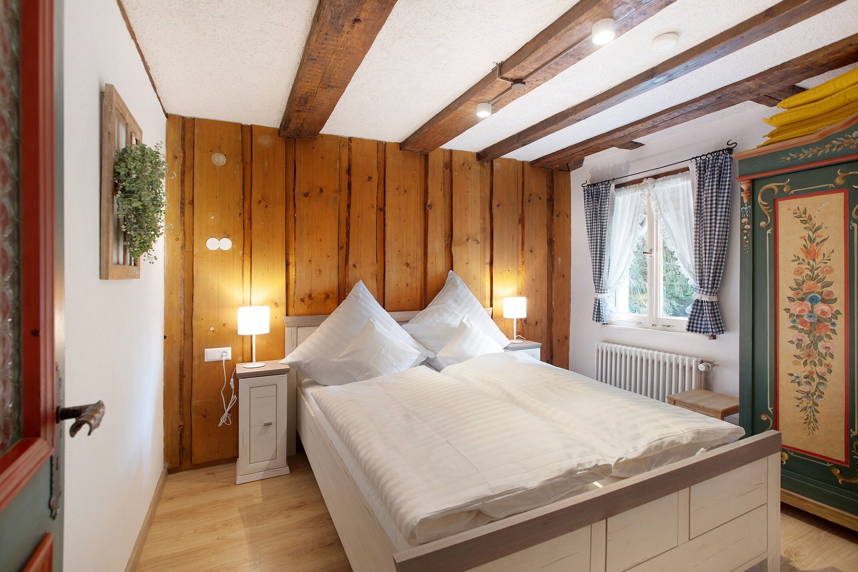 A wooden-paneled bedroom with a bed, bedside lamps, and a window with curtains.
