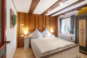 Quarto com painéis de madeira, cama, abajures e janela com cortinas.